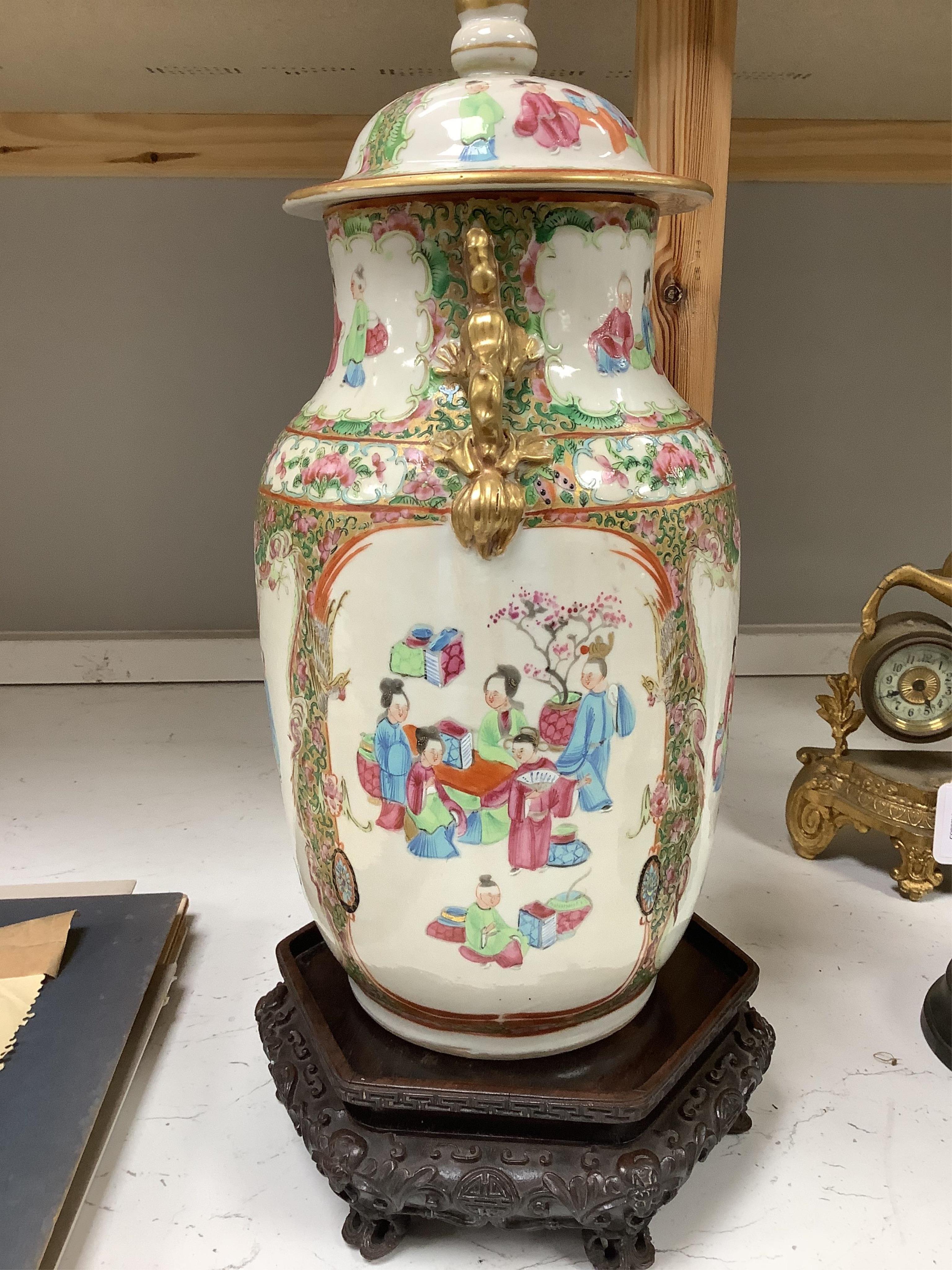 A Chinese famille rose vase and cover, late 19th century, together with a good carved hongmu ‘bats and shou’ stand, vase 36cm. Condition - crack to rim